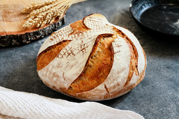 Homemade beautiful loaf of bread and ears of wheat on grey background. Selective focus