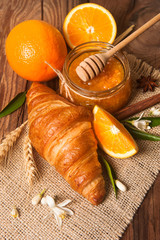 Orange, orange jam and croissant on rustic wood background