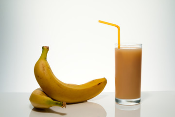 Yellow Ripe bananas from the tropics with banana juice in a glass and a tube for a cocktail, on a light gradient background highlighted with space for text
