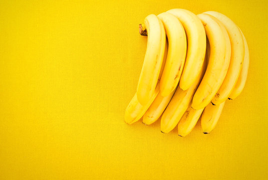 Bunch of yellow ripe bananas from the tropics on a yellow fabric background with space for text