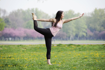 Young woman doing yoga in morning park. Standing half bow pose, utthita ardha dhanurasana. Healthy lifestyle outdoor conception. 