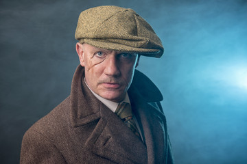 Mature man dressed as an English 1920s gangster, on a blue smoky background