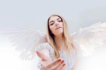 An angel from heaven gives you a hand. Young, wonderful blonde girl in the image of an angel with white wings.