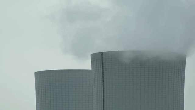 Close up slow pan of the top of two industrial cooling towers producing steam at an electricity generating installation.