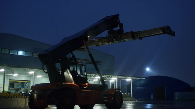 At Night Reach Stacker Driving in Working Area near Industrial Warehoses. Shot on RED EPIC-W 8K Helium Cinema Camera.