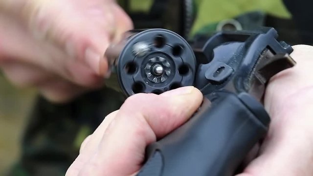 Man holds in hands and cleans revolver drum. Rifleman holds in hands revolver with flobert cartridges. Man turns cylinder of black revolver. Man with black gun, close up