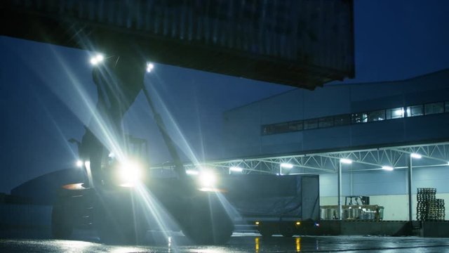 At Night Reach Stacker Driving with Loaded Container in Working Area near Industrial Warehoses. Shot on RED EPIC-W 8K Helium Cinema Camera.