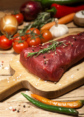 Raw beef steak on a cutting board with rosemary and spices.