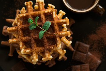 Stack Belgian waffles iced cocoa with chocolate sauce decorated mint leaves on dark wooden background. Selective focus