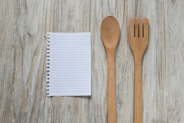 Wooden spoon and spatula with a sheet of paper on wooden background