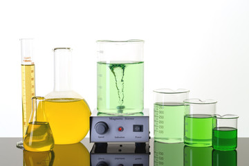Magnetic stirrer, beakers, and erlenmeyer  flask on the table with green and yellow liquids. ...