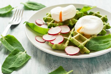Healthy breakfast: spinach waffles with radish slices and poached eggs on green wooden table. Selective focus