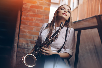 Young attractive girl in white shirt with a saxophone - outdoor. Sexy young woman with sax thinking...