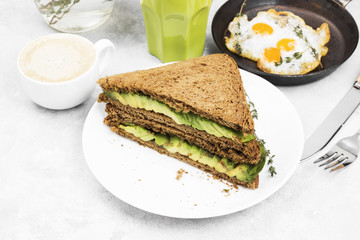 Breakfast - a toast from rye bread with avocado, fried eggs, lemonade and coffee on a light background