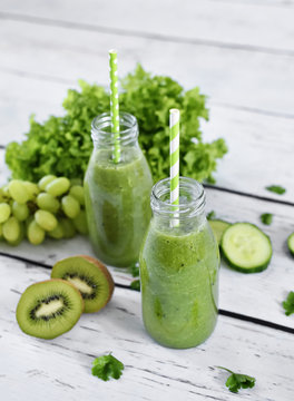 Green smoothie, healthy, organic drinks with fresh vegetables and fruits. Two smoothie glasses with drinking straw on a white table. Close-up shot.