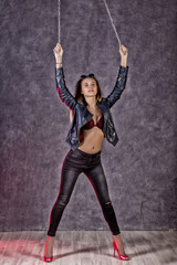 Fototapeta na wymiar Beautiful urban trendy girl in black leather jacket and jeans holding on to chains