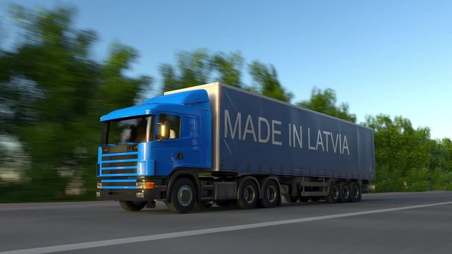 Speeding freight semi truck with MADE IN LATVIA caption on the trailer. Road cargo transportation. Seamless loop 4K clip