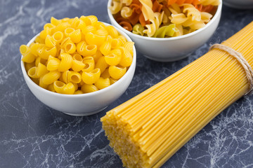 Variety of types of dry Italian pasta on blue marble table. Background