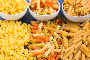 Variety of types of dry Italian pasta on blue marble table. Background