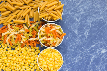 Variety of types of dry Italian pasta on blue marble table. Background
