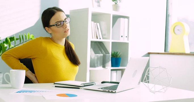 Young business woman with back and neck pain at the office. Woman having back ache while working with laptop computer at the office. Suffering from neck ache. Close up