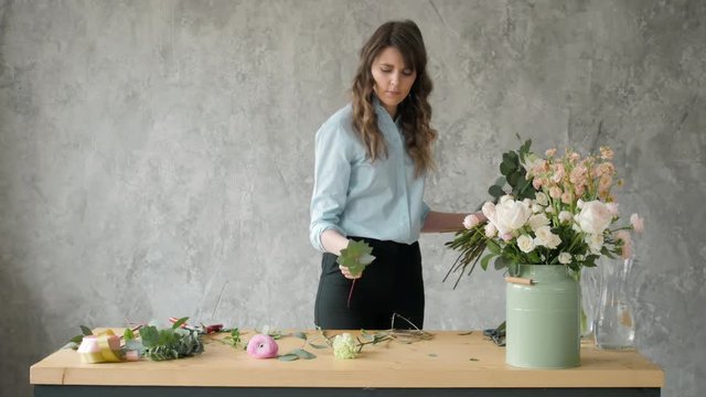 people, business, sale and floristry concept - happy smiling florist woman making bunch at flower shop, bouquet with peone and roses