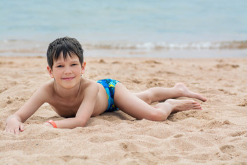 Cute little boy lies on the sand on the seashore happy