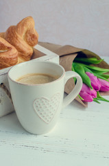 Cup of coffee with bouquet of pink tulips and croissants