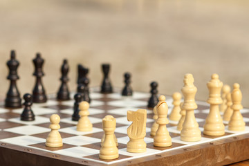 Close up wooden chess pieces on board, selective focus on white knight. Outdoors chess game