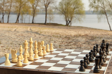 Chess board with chess pieces on river embankment. Outdoors chess game