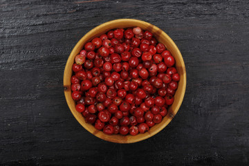 Pink peppercorn in wooden cup on wooden background