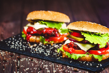 Closeup of home made beef burger with lettuce and potato served on stone cutting board. Dark wooden background