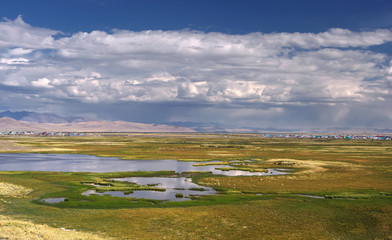 Chuya steppe plateau near village Kosh-Agach with yellow green grass and marsh lakes under a blue sky with white clouds on the background of mountain hills Altai, Siberia, Russia