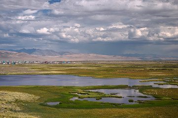 Chuya steppe plateau near village Kosh-Agach with yellow green grass and marsh lakes under a blue sky with white clouds on the background of mountain hills Altai, Siberia, Russia