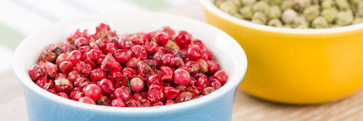 Pink and Green Peppercorns - Bowls filled with dried pink and green peppercorns on a wooden background.