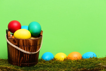 painted easter colorful eggs in wooden bucket with green moss