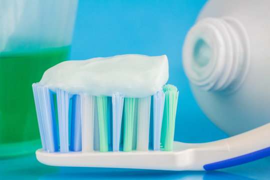 Toothpaste on the toothbrush, green dental rinse, toothpaste tube on blue background, focus on foreground, macro image.