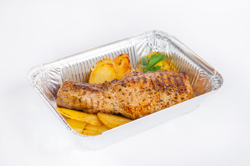 Close up Healthy restaurant food delivery in foil box. Grilled meat steak and Potato Wedges. Meals take away, selective focus. Isolated on the white background.