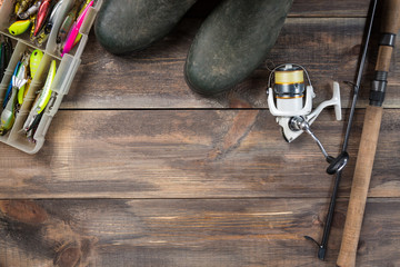 Fishing rods and reel with boots and fishing tackles in a box on wooden background with free space