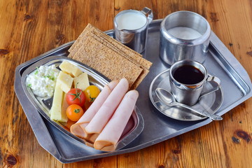 Metal tray with crispbread, cheese, cottage cheese, ham, cherry tomato, cup of coffee, sugar jar, creme jar on a wooden background. Healthy breakfast. Healthy eating