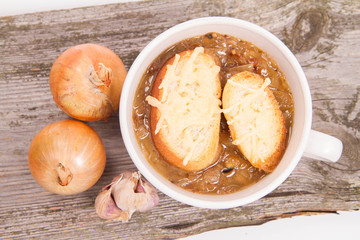 Onion soup with toast on a wooden background with some onions and garlic