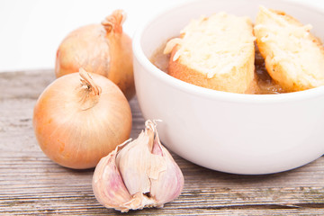 Onion soup with toast on a wooden background with some onions and garlic