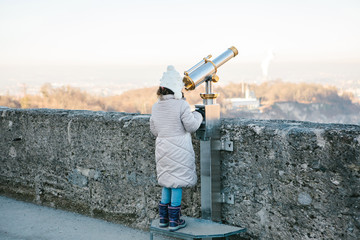 A girl looks through the viewing binoculars on the viewpoint on the hill in the Austrian city of...