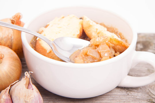 Onion soup with toast on a wooden background being eaten with a spoon