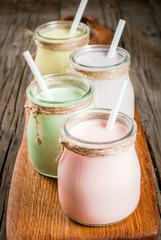 Small jars with a multi-colored smoothie or milkshake - pink cherry, purple berry, green and yellow orange. On a light blue wooden table copy space