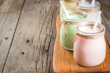 Small jars with a multi-colored smoothie or milkshake - pink cherry, purple berry, green and yellow orange. On a light blue wooden table copy space