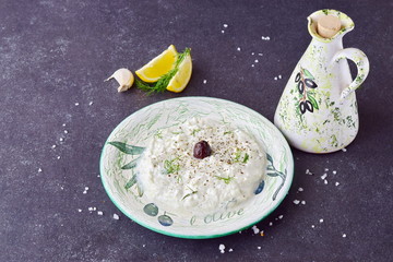 Homemade Greek traditional sauce tzatziki in a traditional colored bowl and a traditional jar with olive oil on a dark abstract background. Healthy eating concept. Mediterranean lifestyle
