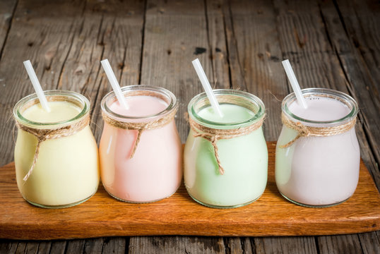 Small jars with a multi-colored smoothie or milkshake - pink cherry, purple berry, green and yellow orange. On a light blue wooden table copy space