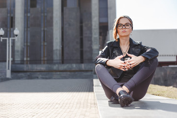 Street fashion concept - stylish cool girl in rock black style sitting among urban background outdoor