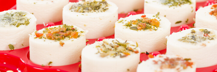 Cheese Appetisers - Soft cheese topped with herbs, spices, and vegetables served on a red tray.